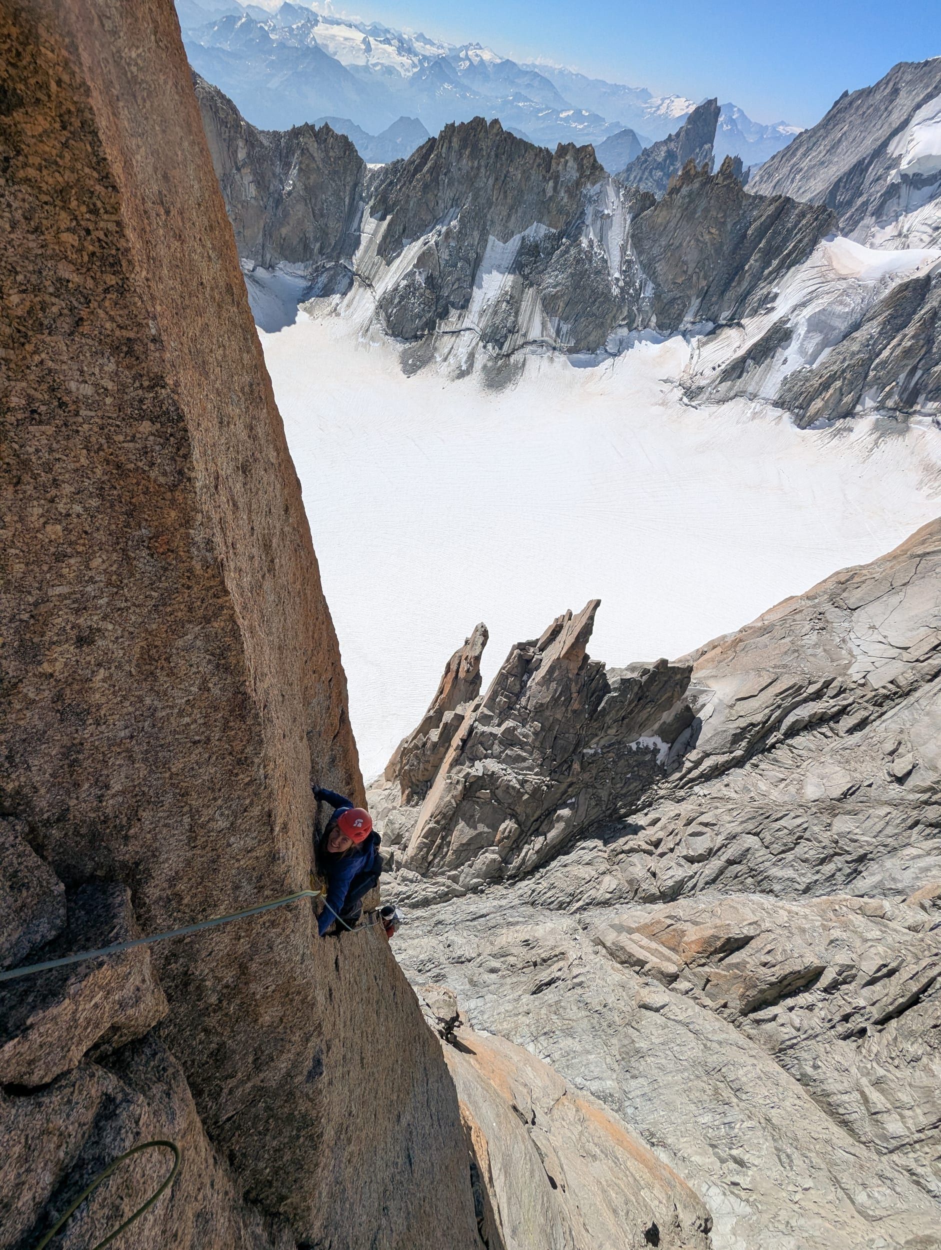 Kletterin lacht in einem Riss, tief unter ihr der Glacier du Géant.